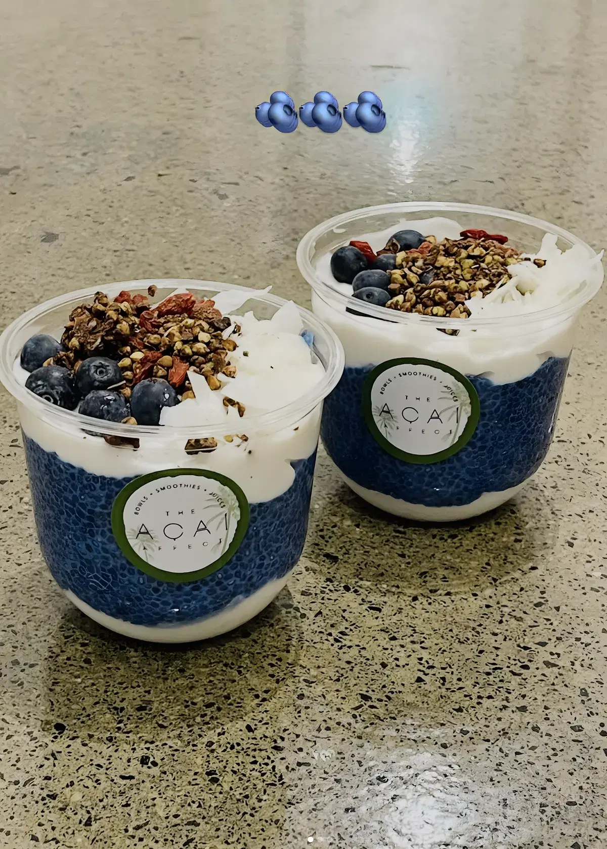 Two blue chia pudding cups topped with blueberries and granola
