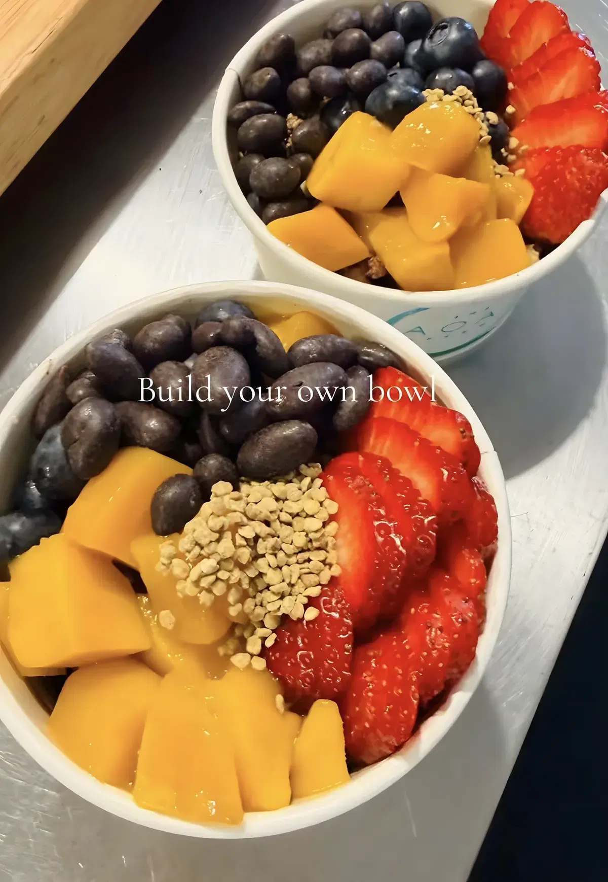 Two build-your-own acai bowls topped with mango, strawberries and bee pollen