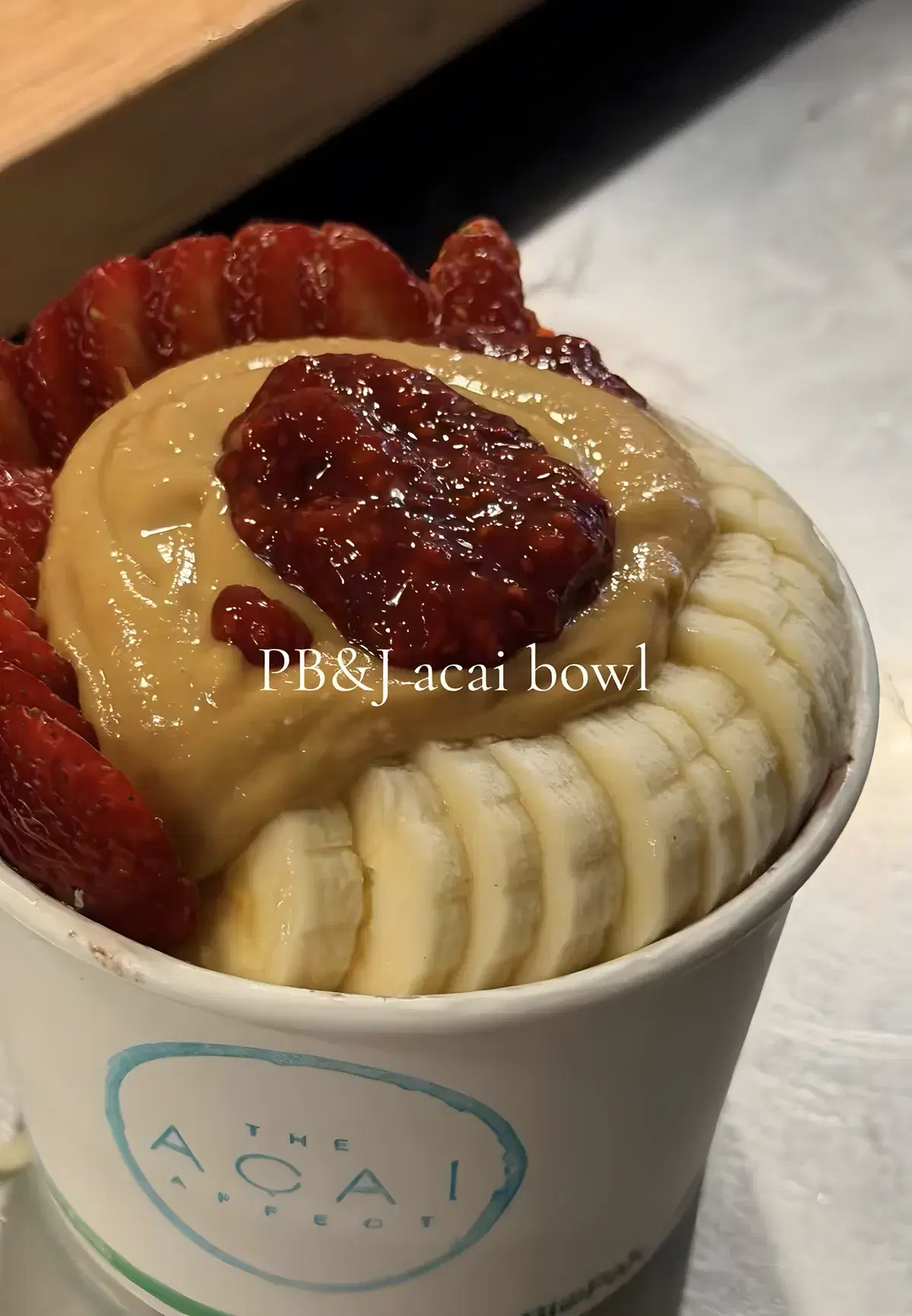 PB&J acai bowl in a takeaway cup with peanut butter, strawberries and sliced banana