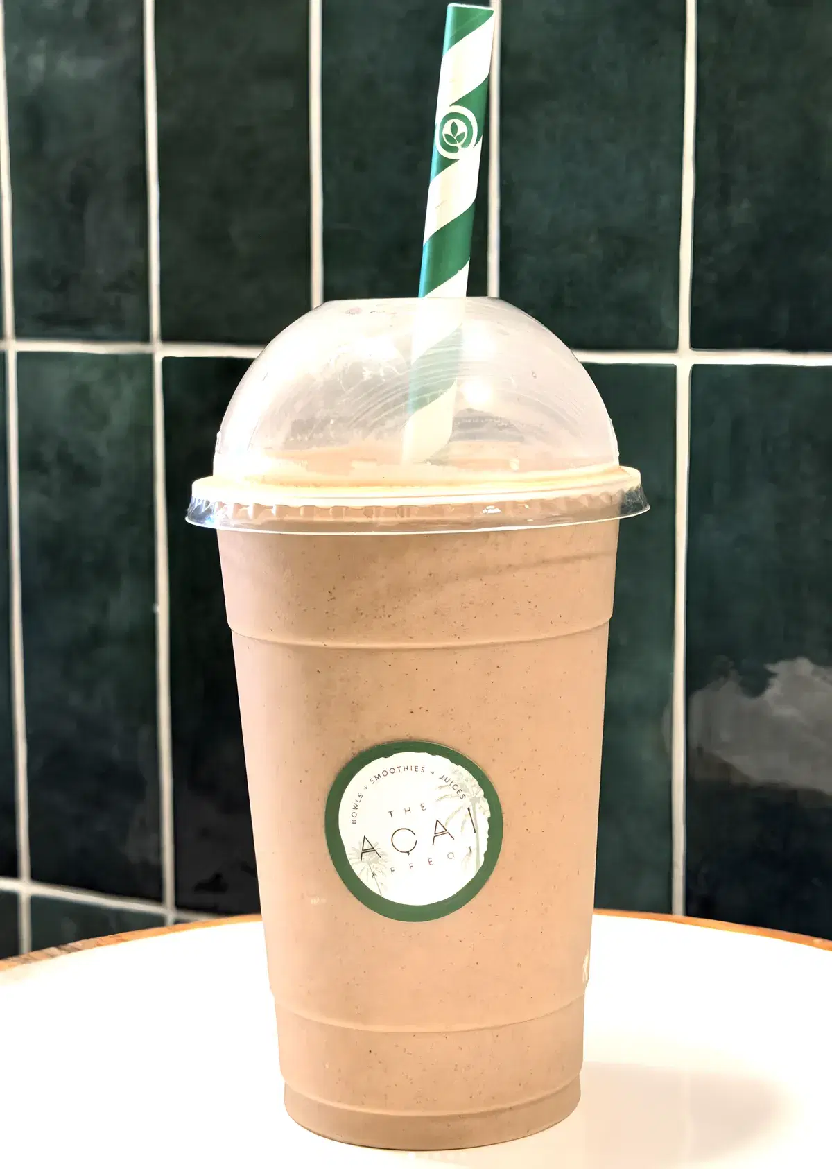 A blended smoothie with a striped straw in front of the shop's green tiles