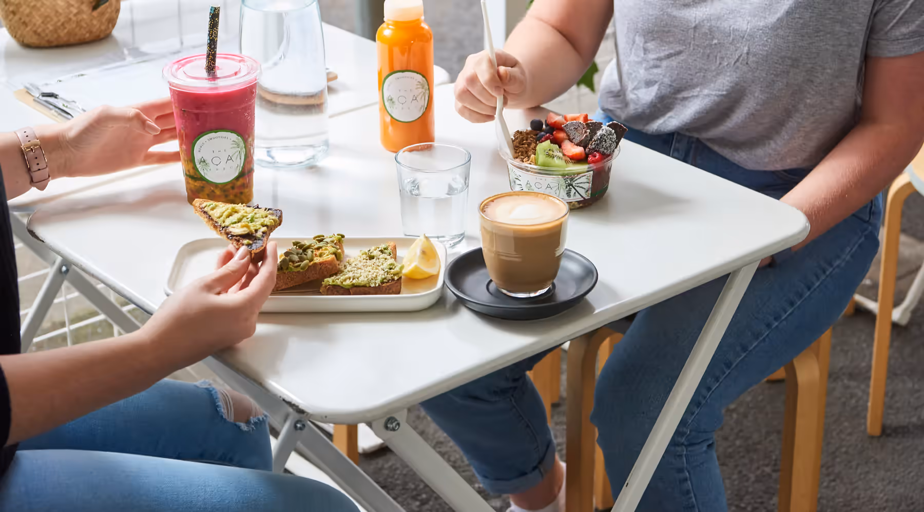 Friends sharing toasts, coffee, a smoothie and an acai bowl at a cafe table