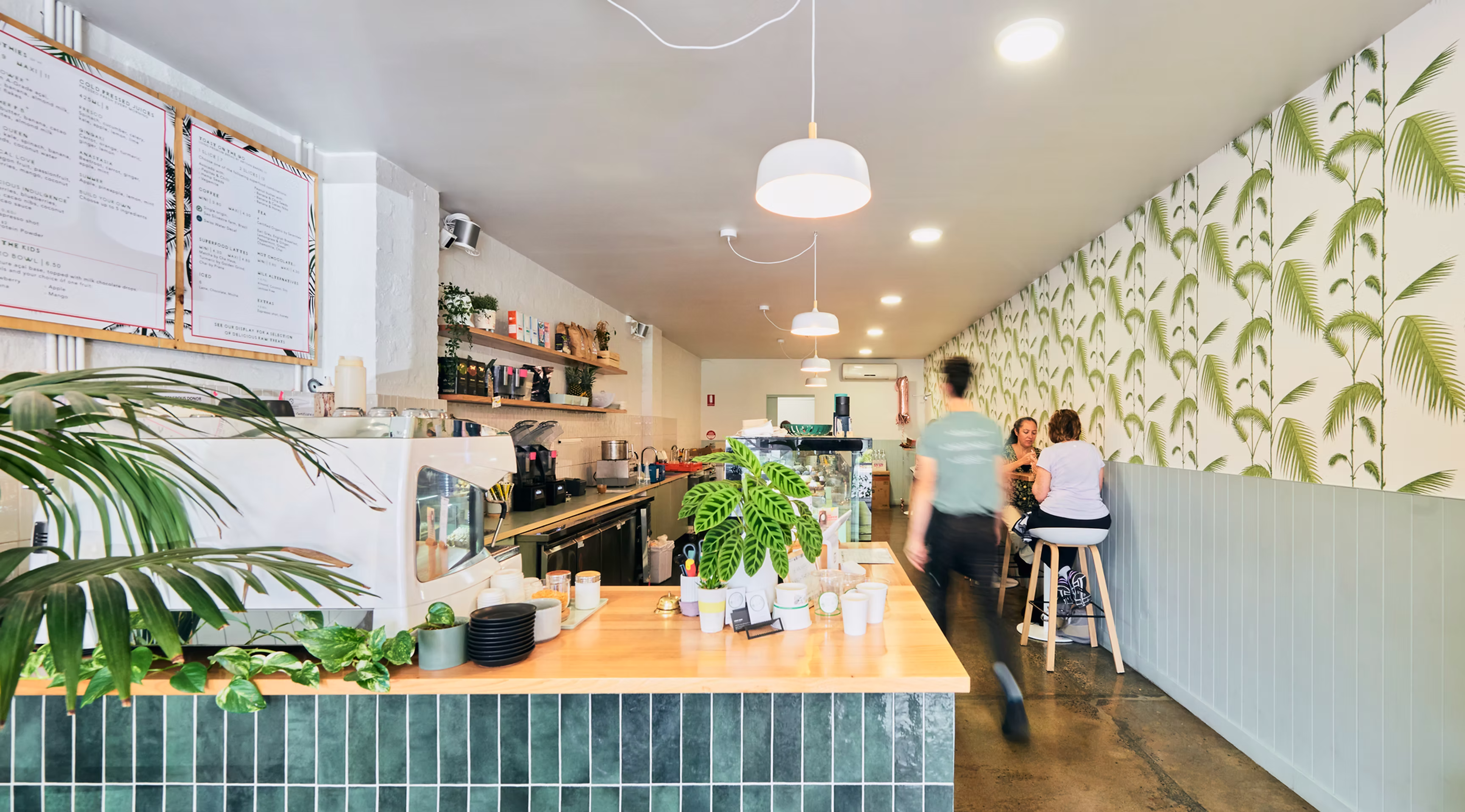 Inside The Acai Affect cafe, with a tiled counter, plants and palm wallpaper